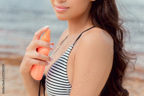 cropped view of girl in swimsuit applying sunscreen