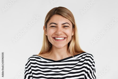 Aattractive cheerful young European woman in striped top expressing joy and good positive emotions, smiling broadly, showing her perfect white teeth, posing isolated at blank copyspace studio wall © shurkin_son
