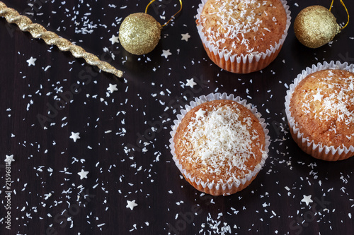 Three homemade muffins decorate coconut powder dark wooden background. New year and Christmas concept.