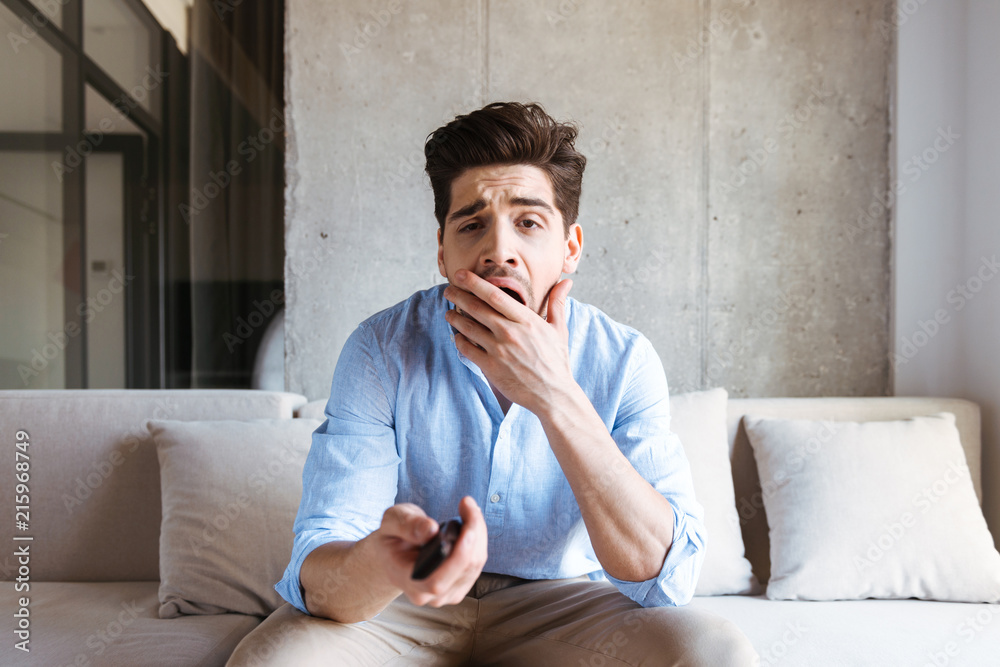 Bored young man holding tv remote control Bored young man holding tv remote control