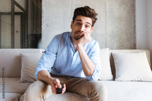 Bored young man holding tv remote control photo