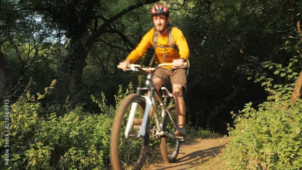 Young male on bicycle with helmet and backpack ride alone in the forest Young male on bicycle with helmet and backpack ride alone in the forest