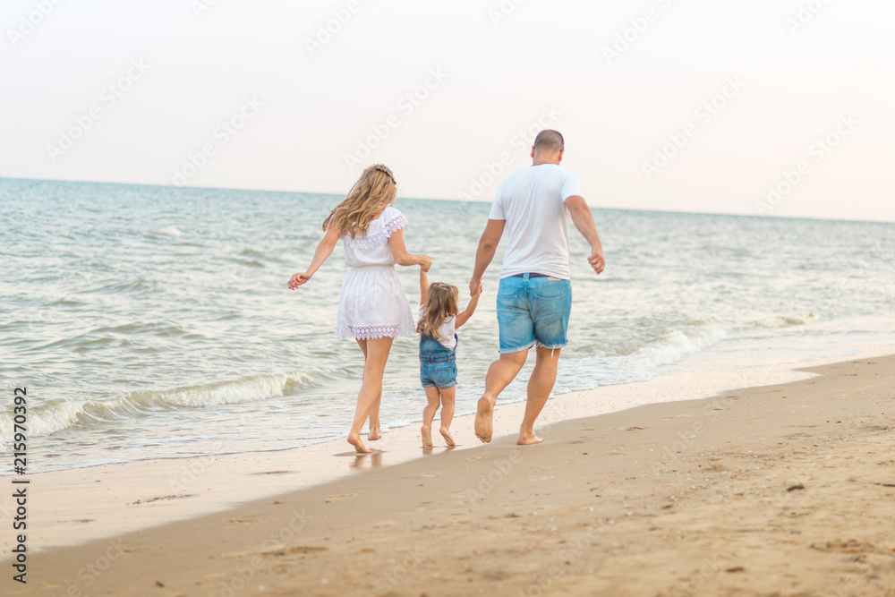 Close up Happy family of three - beatiful wife, father and daughter having fun walking on beach at sunset. Family traveling concept.