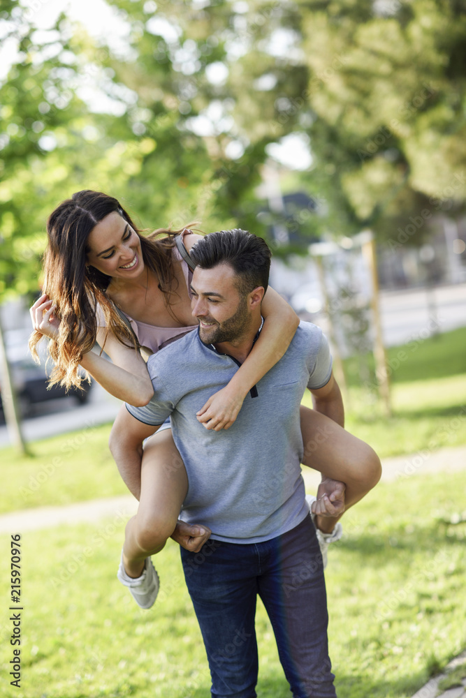 Happy man giving girlfriend a piggyback ride in park Happy man giving girlfriend a piggyback ride in park
