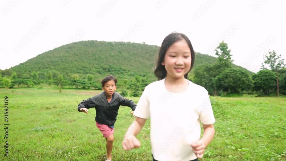 Slow motion of young Asian kids run on a green field near a hill in summer day Slow motion of young Asian kids run on a green field near a hill in summer day