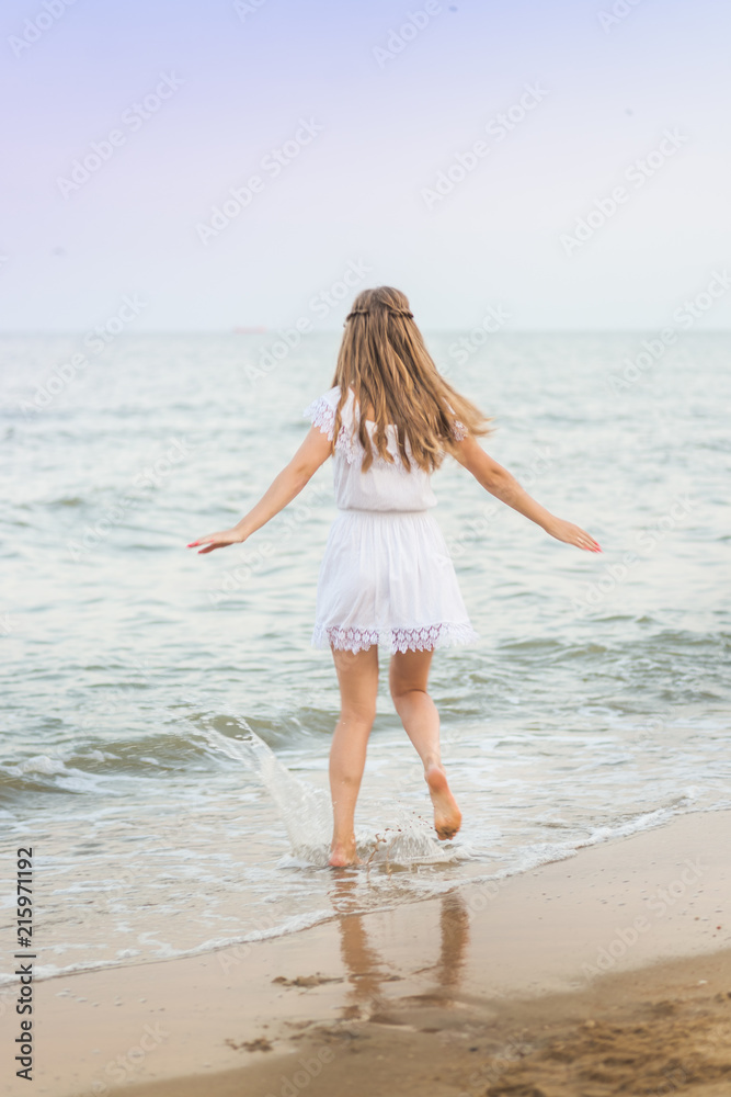 A beautiful model in a white dress is sexually running around on the beach on a beach