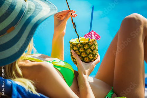 Portrait of young woman with cocktail glass chilling in the tropical sun near swimming pool on a deck chair