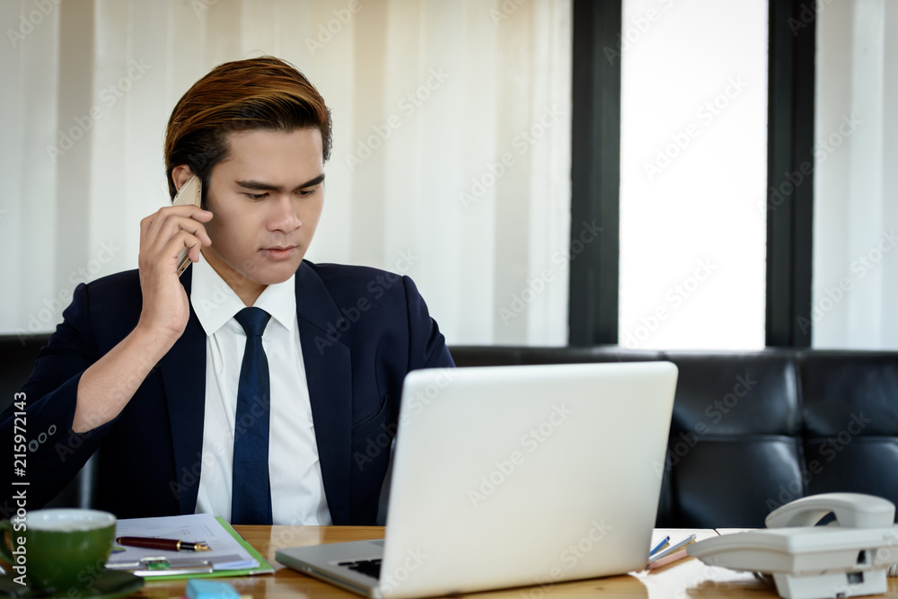 Businessman dressed smart is using a mobile phone to communicate wirelessly. While sitting at work with a laptop in the office. Business and Technology Concepts. Businessman dressed smart is using a mobile phone to communicate wirelessly. While sitting at work with a laptop in the office. Business and Technology Concepts.