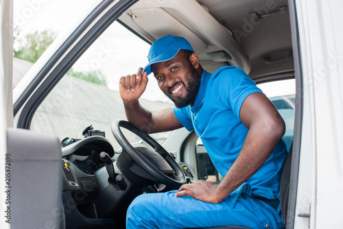 african american delivery man greeting and touching cap in car