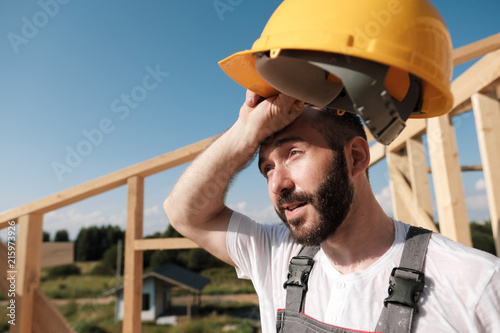 The man is a builder on the roof of a wooden frame house.
