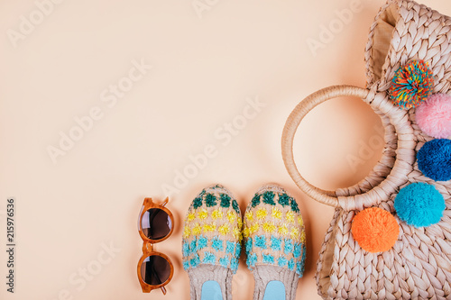 Summer fashion flatlay with brown sunglasses, trendy straw bag with pompoms and gradient espadrille sandals on the beige background. Perfect beach set for holidays on sea. photo