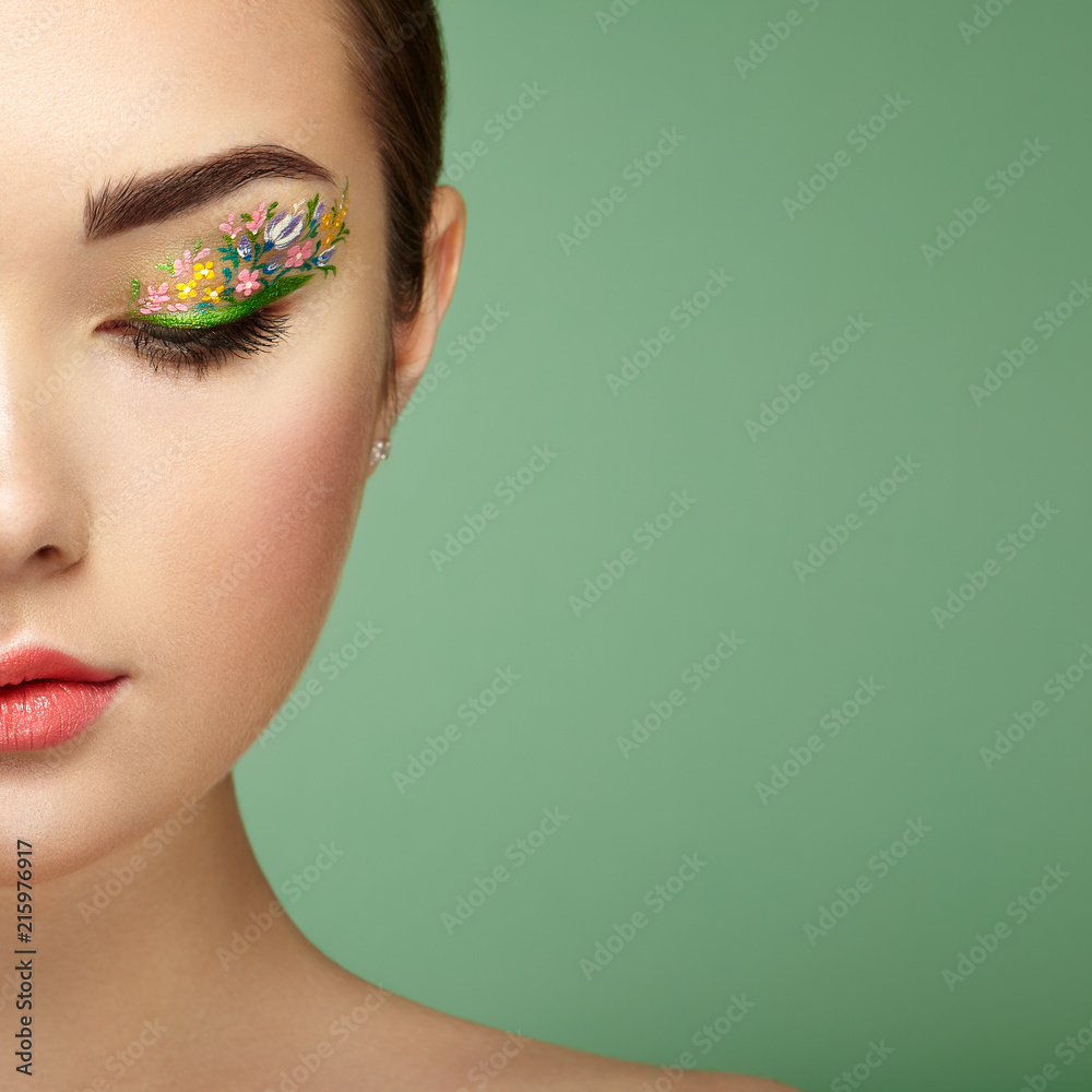 Young beautiful woman with flower makeup eyes. Spring makeup. Beauty fashion. Eyelashes. Cosmetic Eyeshadow. Make-up detail. Girl on green background - obrazy, fototapety, plakaty 