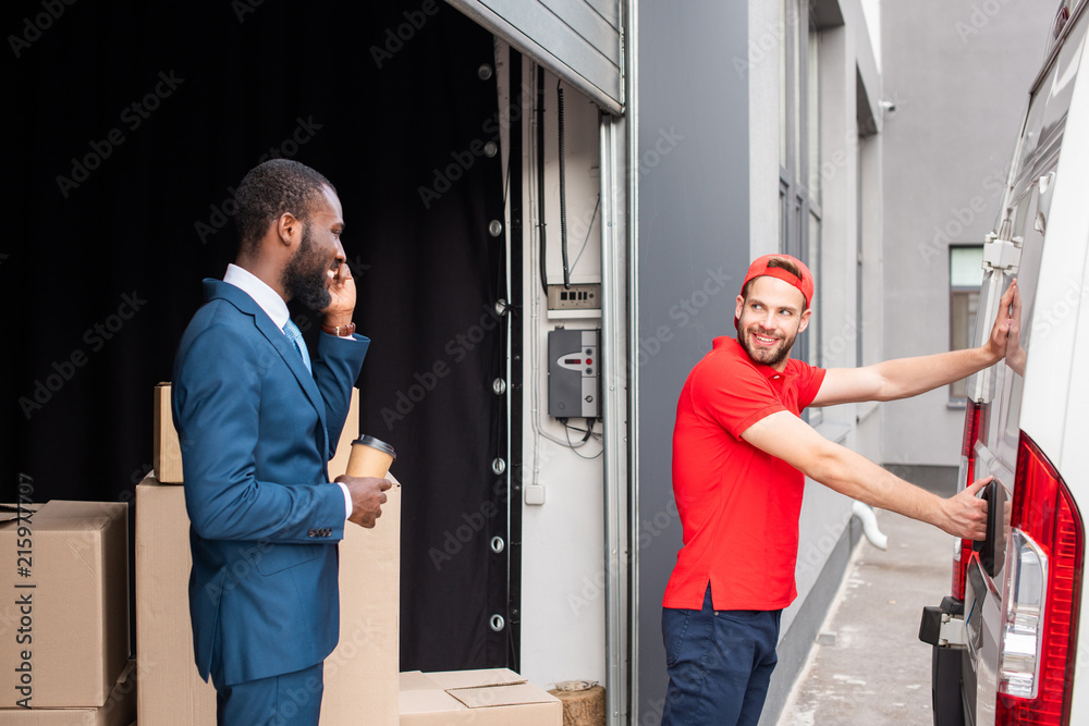 african american businessman with coffee to go controlling caucasian delivery man while talking on smartphone african american businessman with coffee to go controlling caucasian delivery man while talking on smartphone