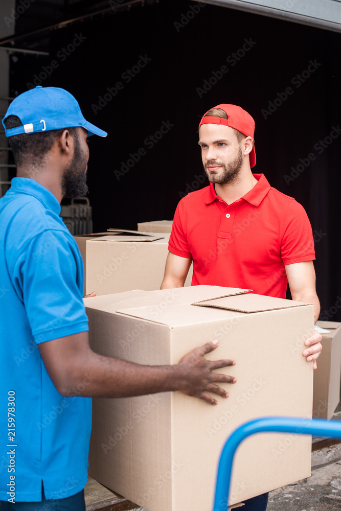 multicultural delivery men in red and blue uniform with cardboard boxes multicultural delivery men in red and blue uniform with cardboard boxes