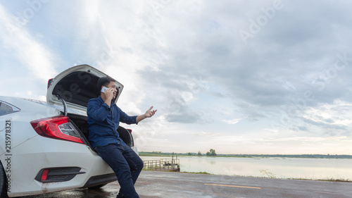 Foto Asian businessmen talking on a cell phone by a broken car On Country Road Phoning For Help