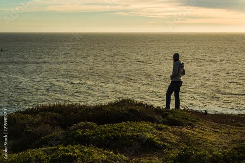 Woman walking along coastal trail taking smartphone photos in silhouette
