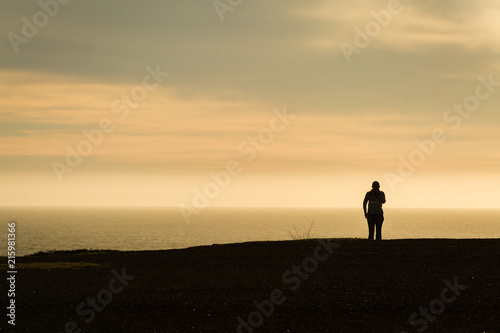 Woman walking along coastal trail taking smartphone photos in silhouette