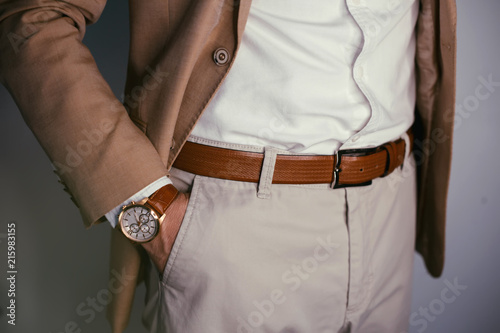 Closeup fashion image of luxury watch on wrist of man.body detail of a business man.Man's hand in brown pants pocket closeup at white background.Man wearing brown jacket and white shirt.Toned. photo