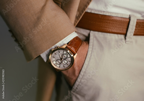 Closeup fashion image of luxury watch on wrist of man.body detail of a business man.Man's hand in brown pants pocket closeup at white background.Man wearing brown jacket and white shirt.Toned. photo