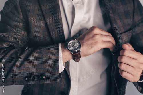 Closeup fashion image of luxury watch on wrist of man.body detail of a business man.Man's hand in brown pants pocket closeup at white background.Man wearing brown jacket and white shirt.Toned.