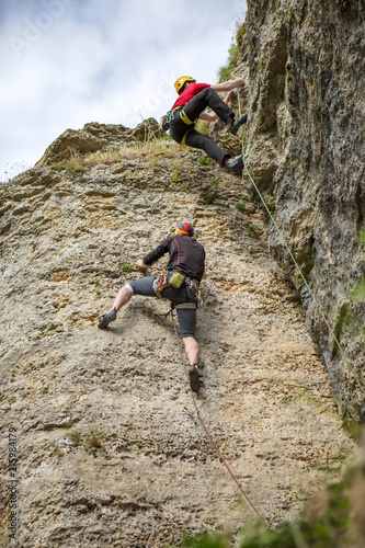 Photo from back of climbing young sports men in helmet on rock