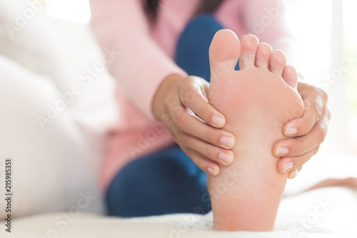 Closeup woman sitting on sofa holds her foot injury  feeling pain. Health care and medical concept.