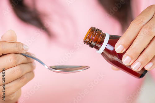 Woman hand pouring medication or antipyretic syrup from bottle to spoon. healthcare, people and medicine concept.