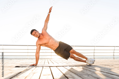 Sportsman outdoors on the beach make exercises on sport carpet.