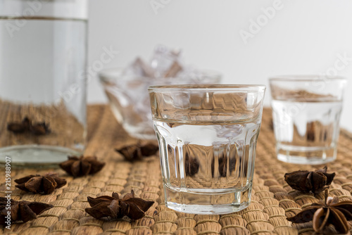 Glasses and bottle of traditional drink Ouzo or Raki with anise star seeds on natural matting photo