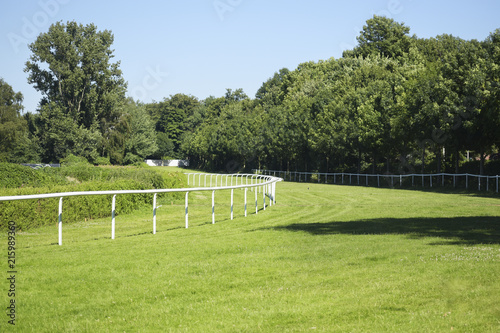 Empty horse racecourse, treated green grass and white rails at the racing track, background landscape with copy space