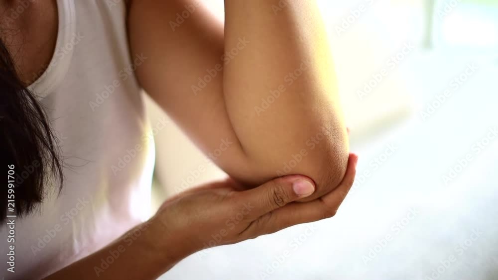 Closeup young woman sitting on sofa and feeling elbow pain and she massage her elbow at home. Healthcare and medical concept. Closeup young woman sitting on sofa and feeling elbow pain and she massage her elbow at home. Healthcare and medical concept.