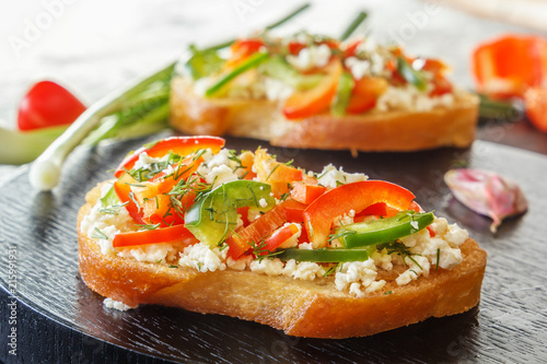 Bruschetta with red sweet pepper and goat cheese on a black plate. Close-up