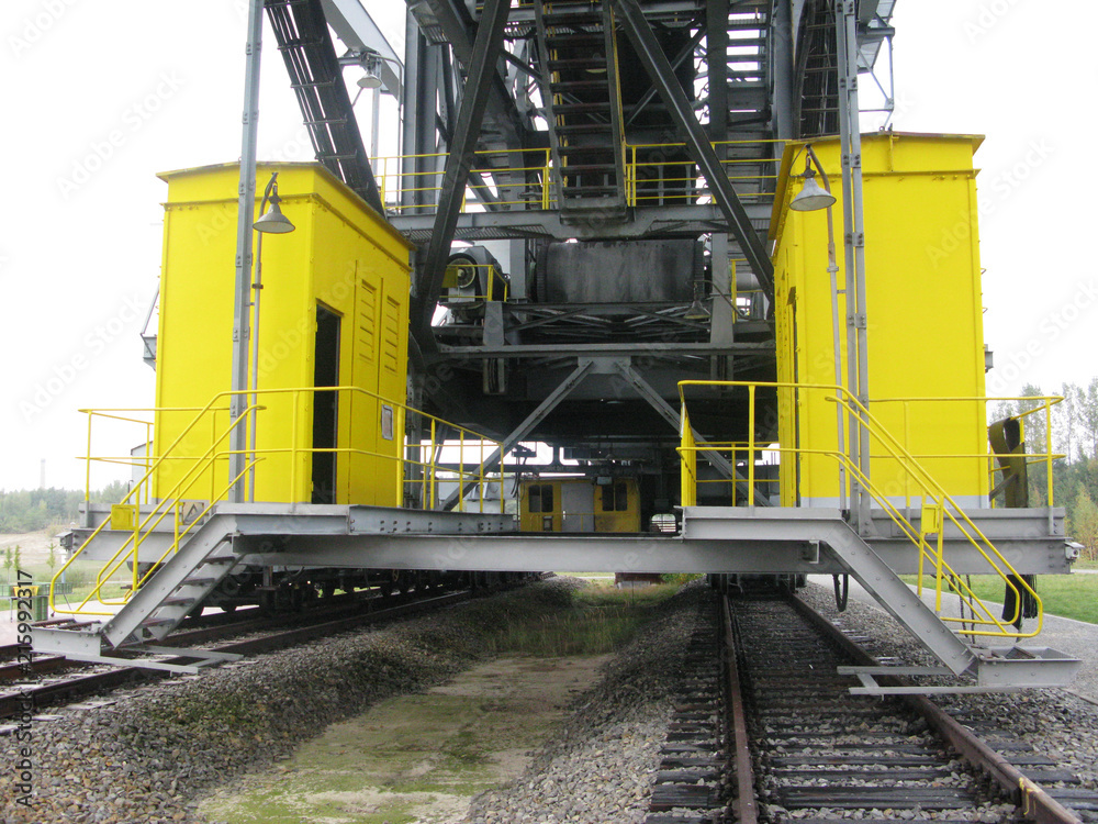 yellow steel cabins on a platform, steel ladders, traverses, beams, steel stairs and tracks, working place a sparse landscape with trees on horizon, industrial building site