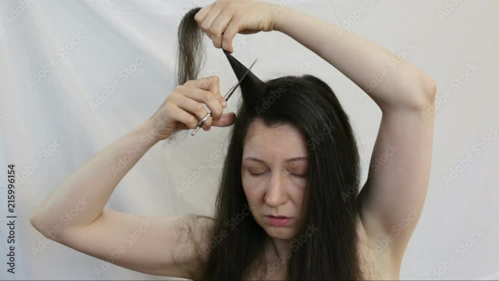 Girl decides as short it cut off their long dark hair. Woman holding a strand of hair and scissors cuts them very short. Real time, indoors, close-up,