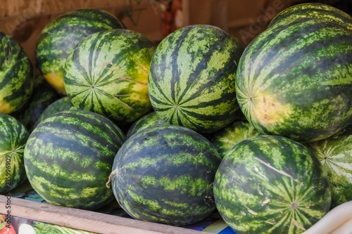 Pile of fresh ripe watermelons lying in wooden boxes in fruit and vegetable department of supermarket.