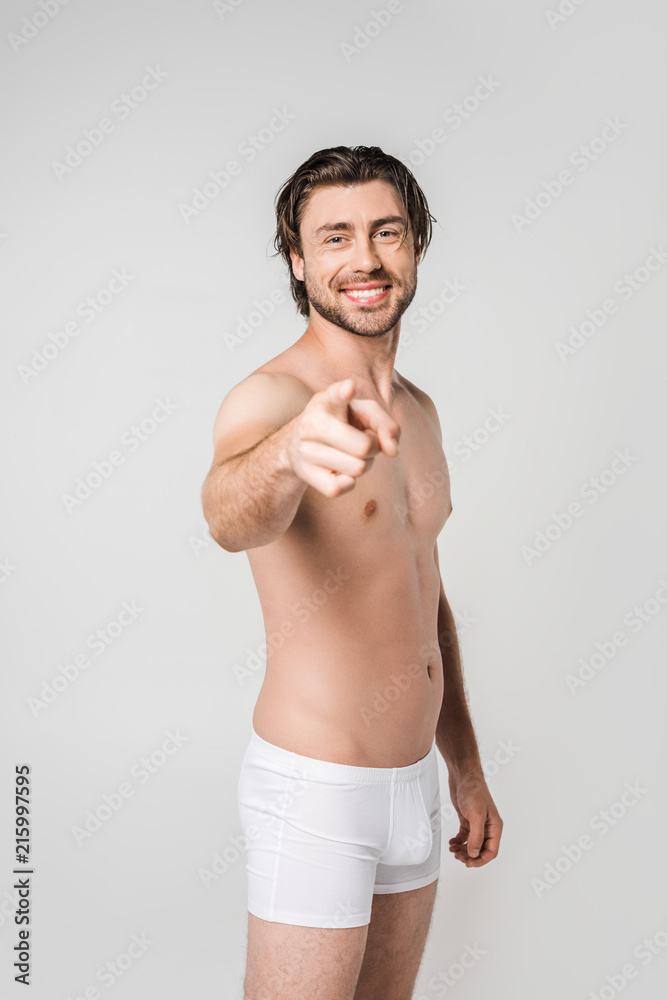 portrait of smiling man in white underwear pointing at camera isolated on grey