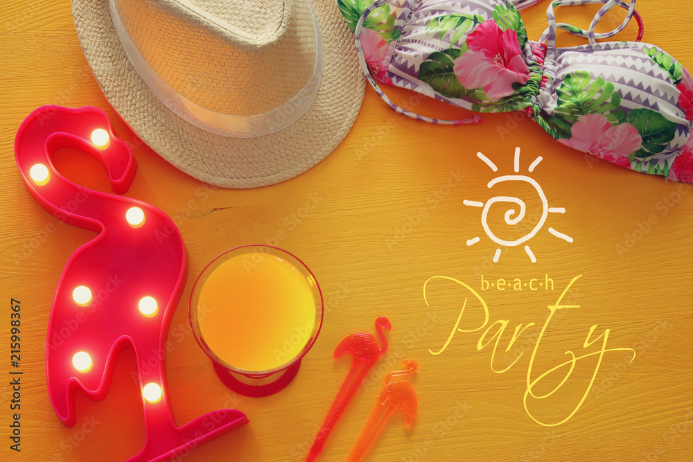 Top view of fashion female swimsuit bikini and white fedora hat over yellow wooden background. Summer beach vacation concept. Top view of fashion female swimsuit bikini and white fedora hat over yellow wooden background. Summer beach vacation concept.