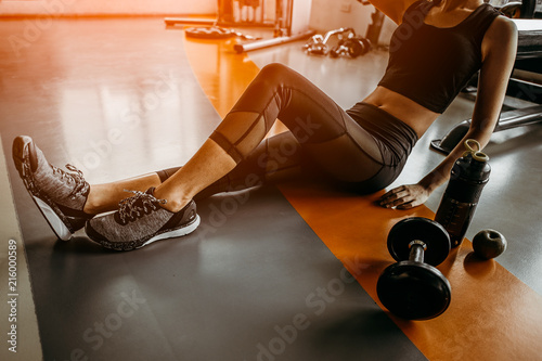 Fototapeta Naklejka Na Ścianę i Meble -  Relaxing after training.young woman sitting with dumbbell and protein shake bottle at gym.young female at gym taking a break from workout.