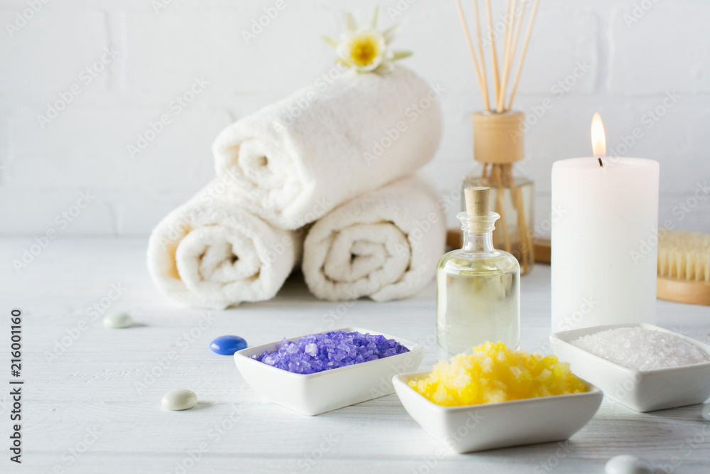 Spa still life with towel,white lily, sea salt, bath oil, sugar body scrub, massage brush and candle