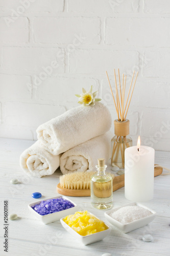 Spa still life with towel,white lily, sea salt, bath oil, sugar body scrub, massage brush and candle