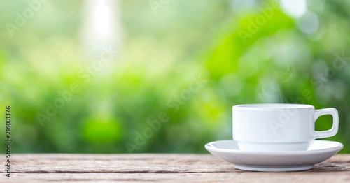 Coffee cup on wooden table or counter with green nature light blur background