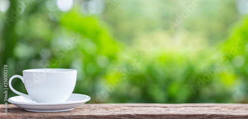 Coffee cup on wooden table or counter with green nature light blur background