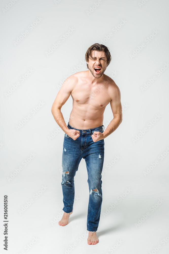emotional shirtless man in jeans showing muscles on grey backdrop