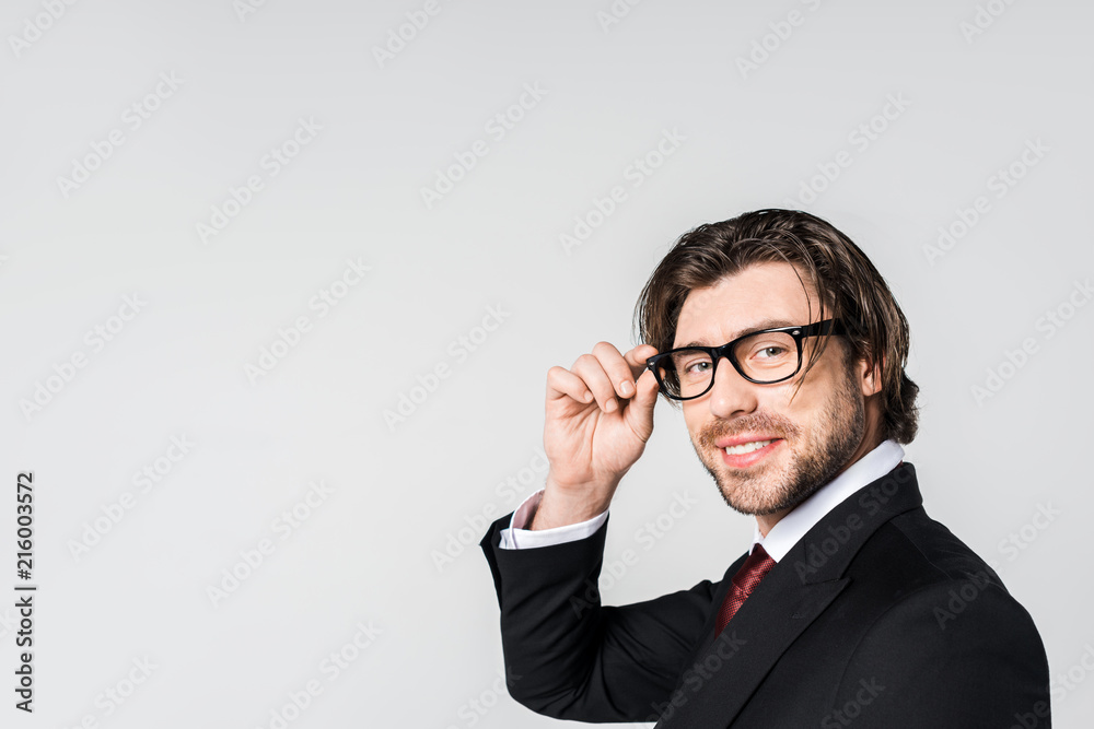 side view of smiling businessman in stylish suit and eyeglasses looking at camera isolated on grey side view of smiling businessman in stylish suit and eyeglasses looking at camera isolated on grey
