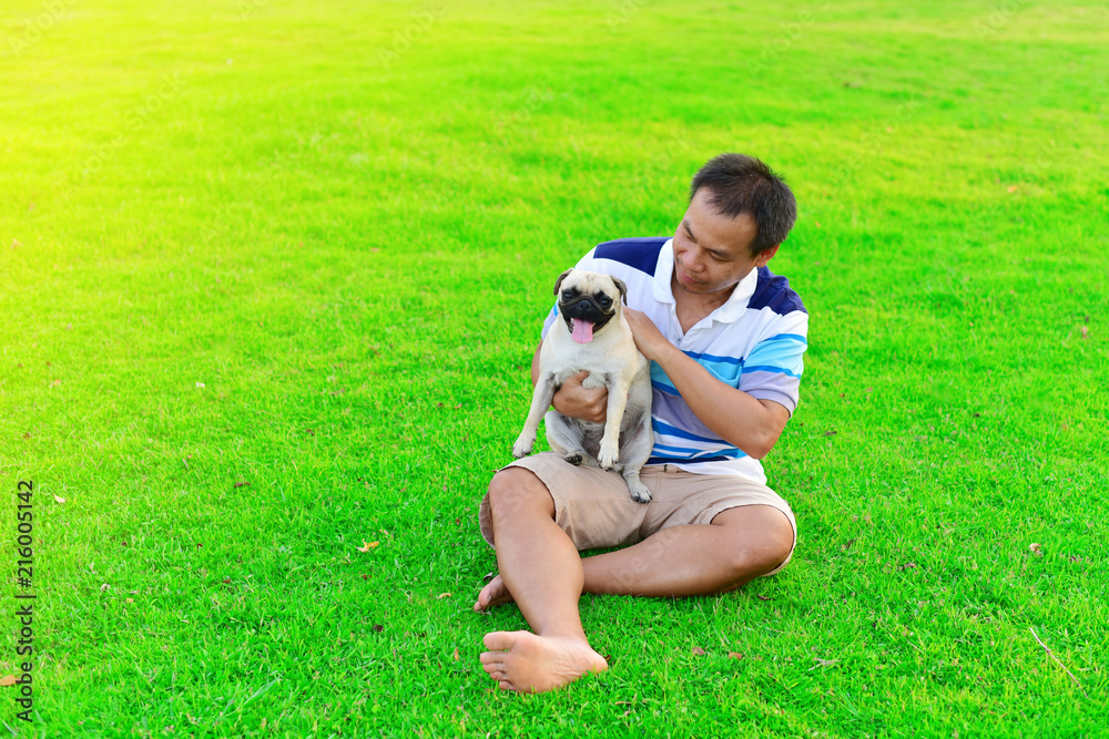 Happy Asian man playing with brown Pug in garden
