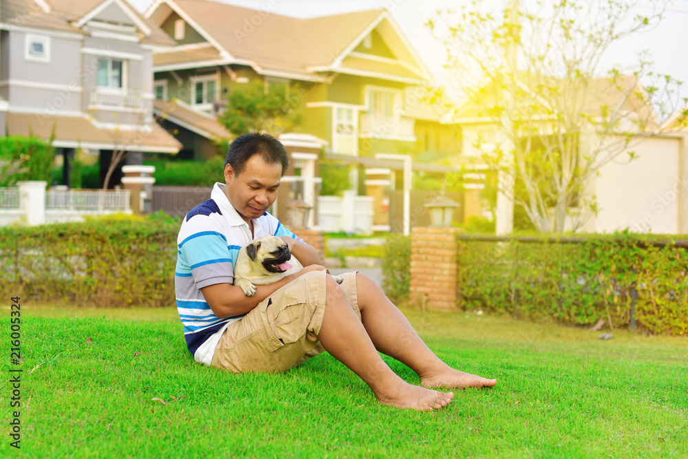 Happy Asian man playing with brown Pug in garden

