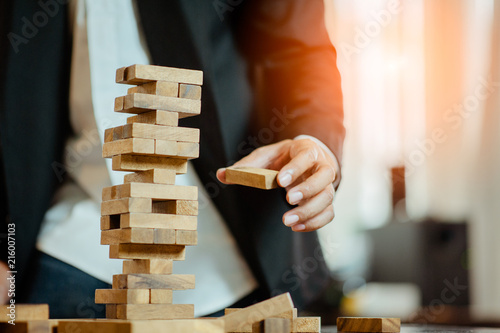 business man hand pulling out or placing wood block on the tower in modern office. plan and strategy in business. blur for background.