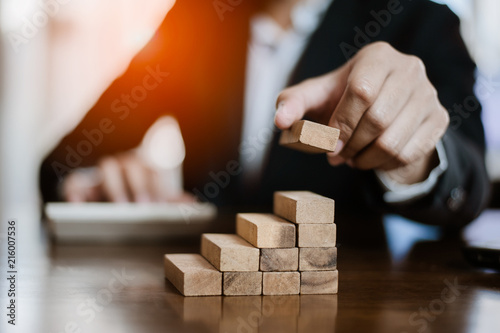 plan and strategy in business.risk concept.hand of man has piling up and stacking a wooden block.Businessman Building The Success.using calculator to calculate.