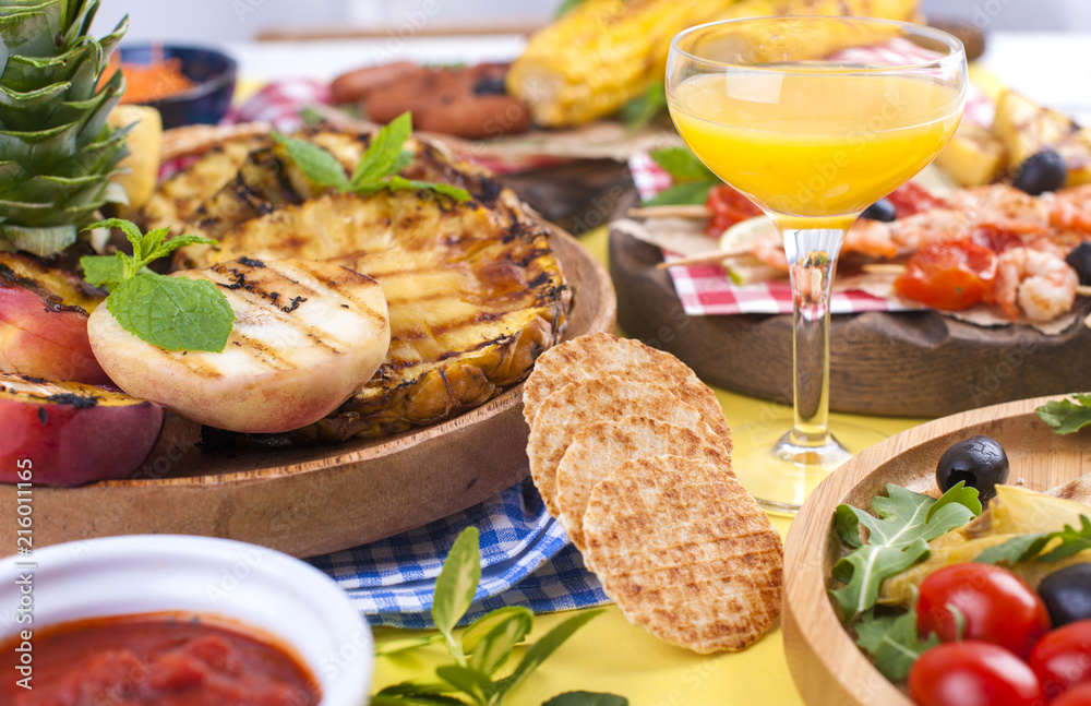 Picnic with grilled food. Sausages and corn on barbecue, shrimp, vegetables and fruits. Delicious summer lunch and plastic dishes. Top view Picnic with grilled food. Sausages and corn on barbecue, shrimp, vegetables and fruits. Delicious summer lunch and plastic dishes. Top view