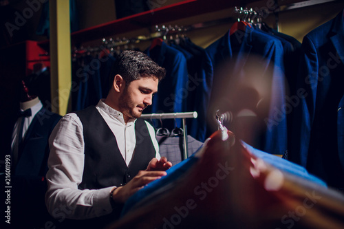 Tailor, tailoring. Men's suit, tailor in his workshop. Elegant man's suits hanging in row. Luxury mens classic suits on rack in elegant men's boutique. photo